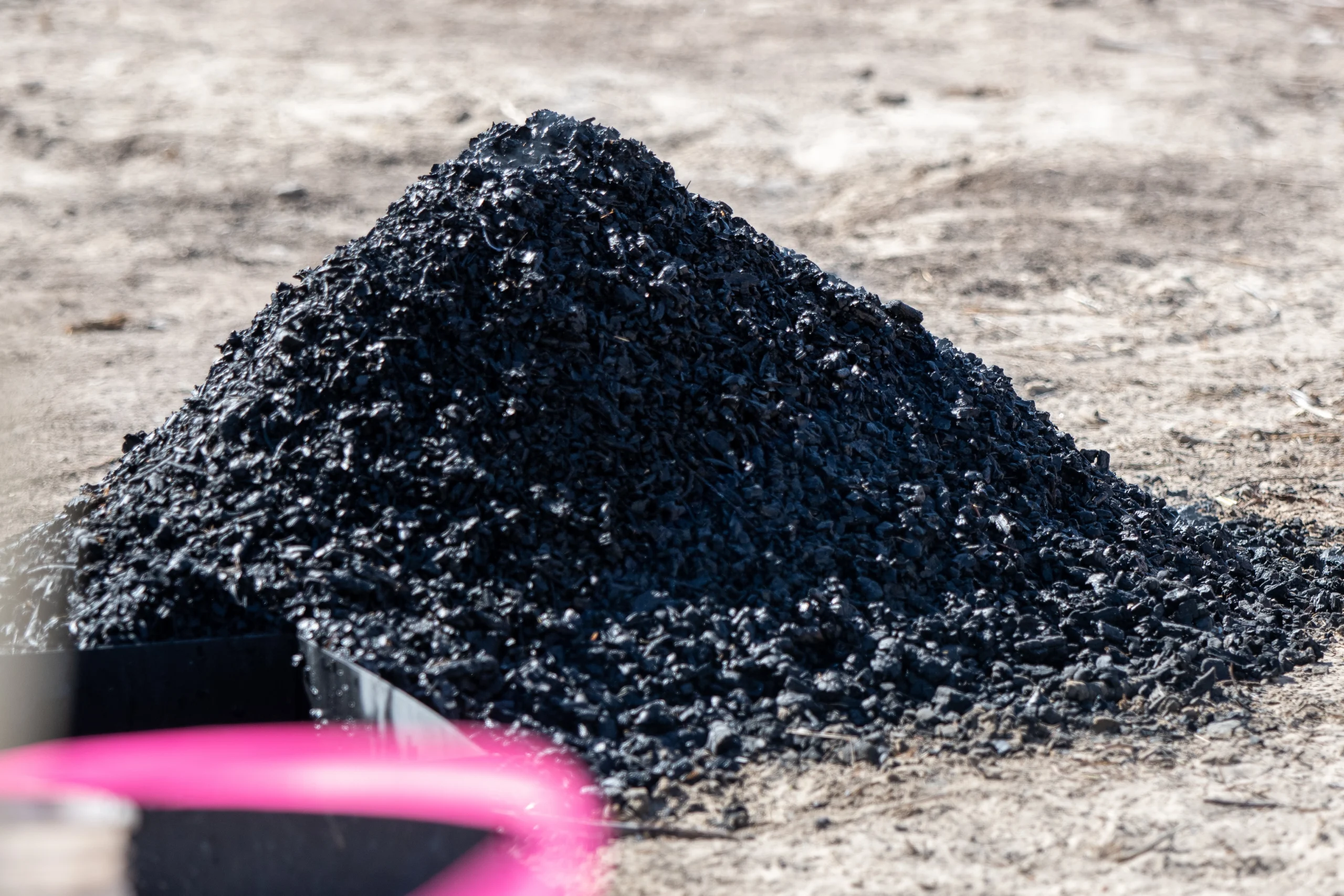 A pile of charred wood sits on a dirt surface