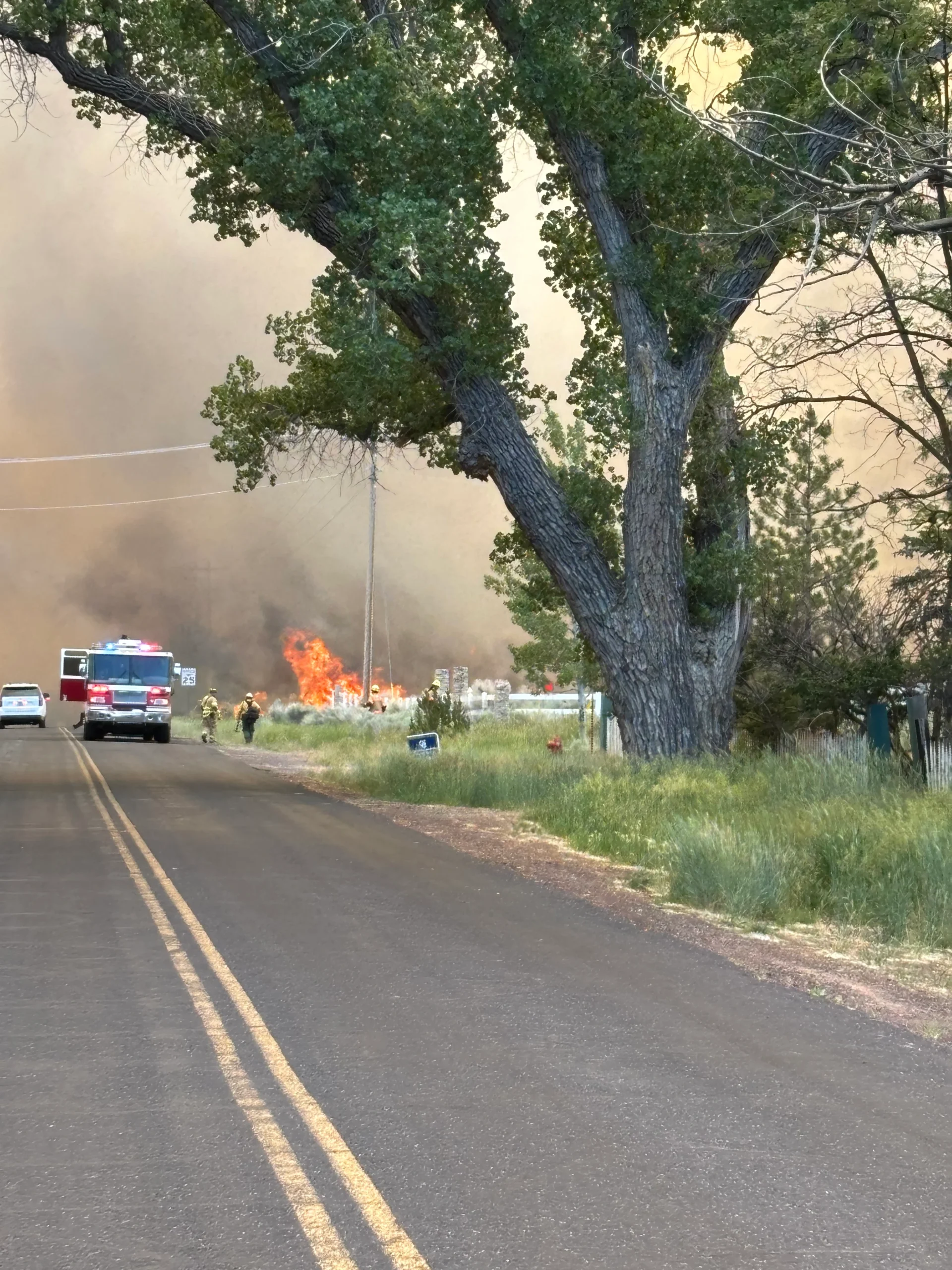 Fire truck and firefighters on road near active fire and heavy smoke